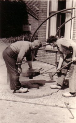 Dolf en zoon Rikus bezig met het omleggen van een metalen wielband om een karre-of kruiwagenwiel. 